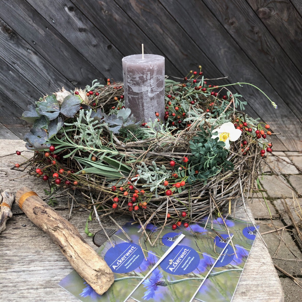 Kerzenkranz aus bunten, herbstlichen Pflanzen mit Flyern des Ackerwert Projekts auf einer Holzbank